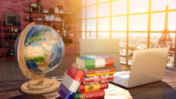 Un bureau sur lequels sont posés une map monde et une pile de dictionnaires dans différentes langues 